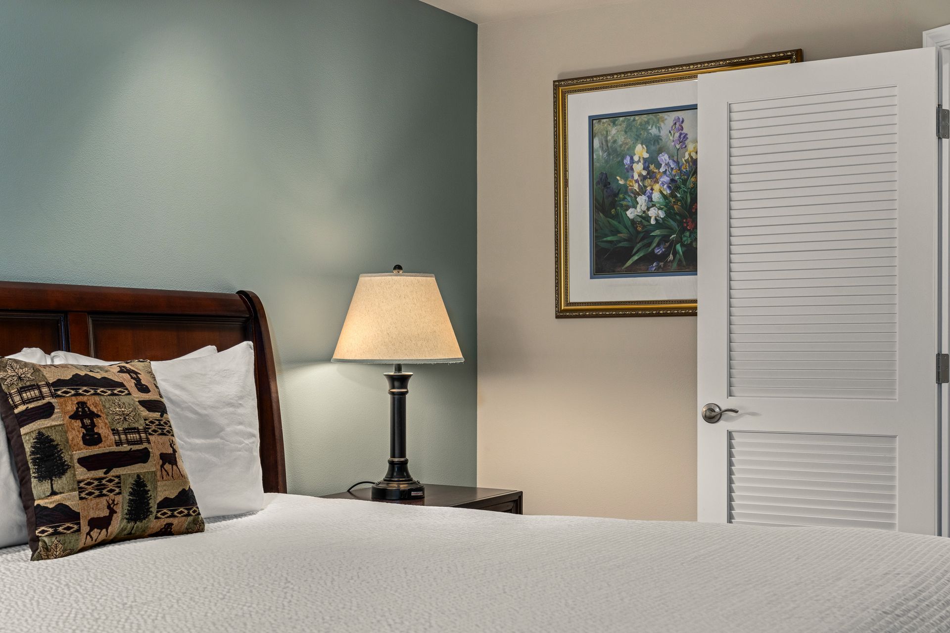 Cozy bedroom with bed, bedside lamp, framed art, and white louvered closet doors.