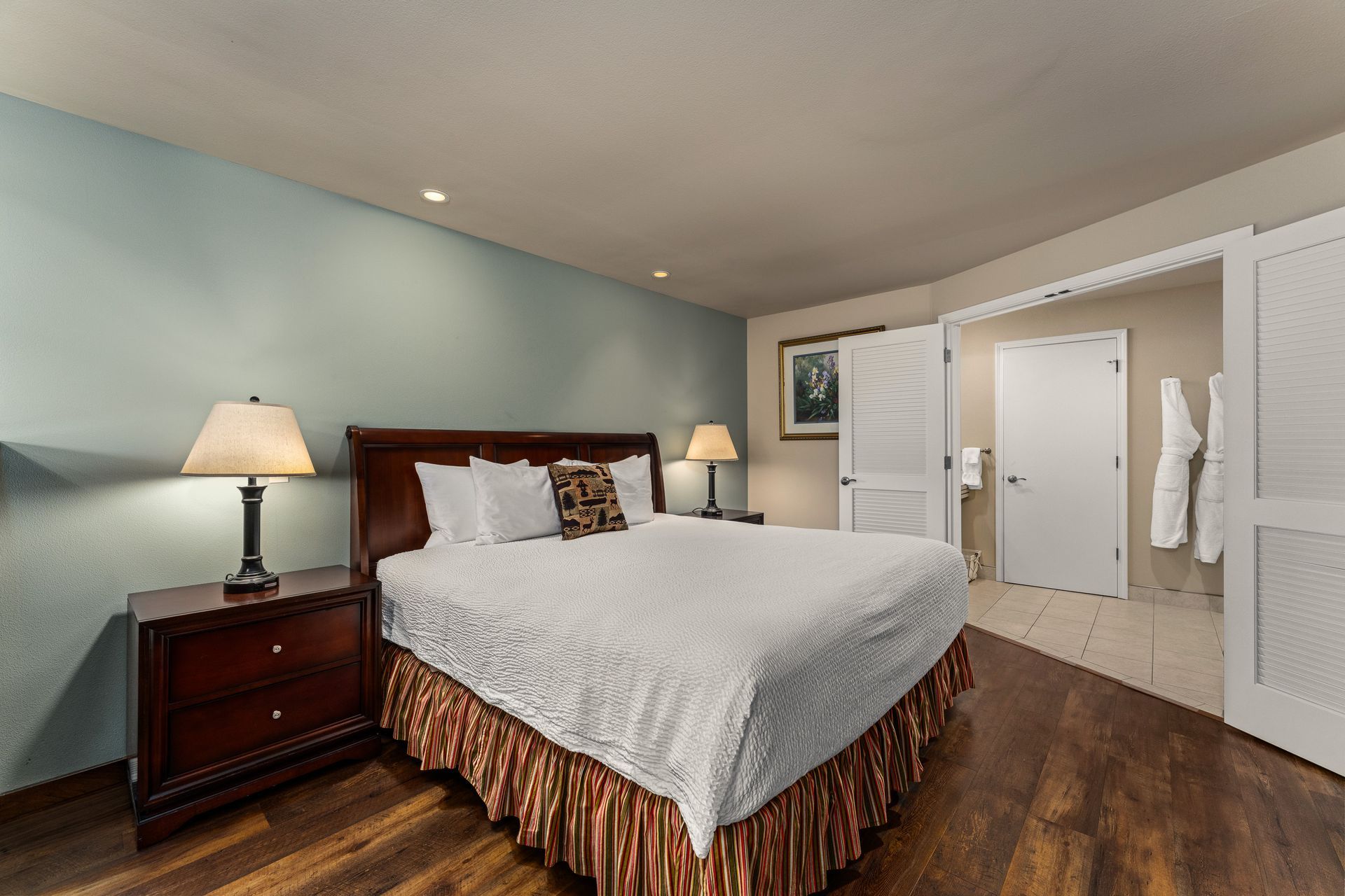 Neatly made bedroom with a large bed, bedside lamps, and hardwood floor