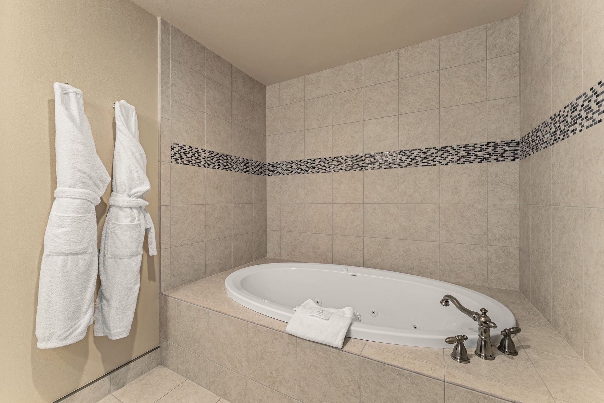 Neutral beige bathroom with a built-in tub, towel rack, and decorative tile border.