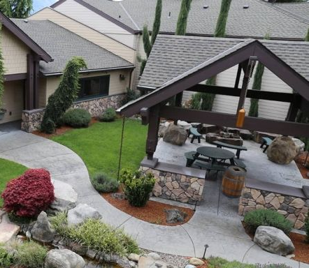 Courtyard patio with stone fire pit, curved walkway, and landscaped shrubs beside homes