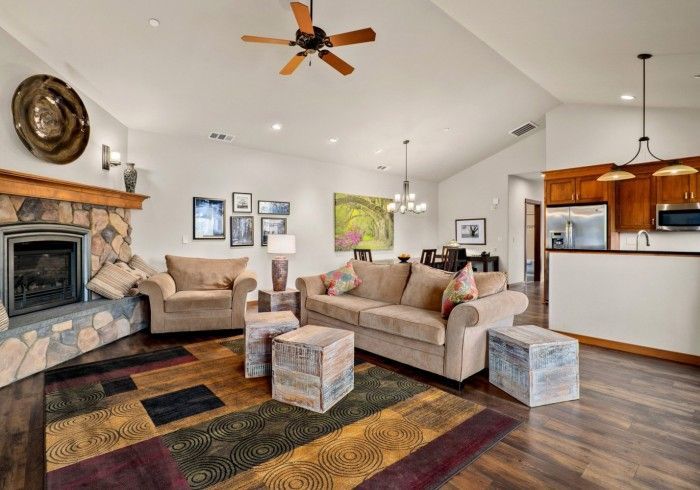 Spacious living room with beige sofas, stone fireplace, colorful rug, and open kitchen view.