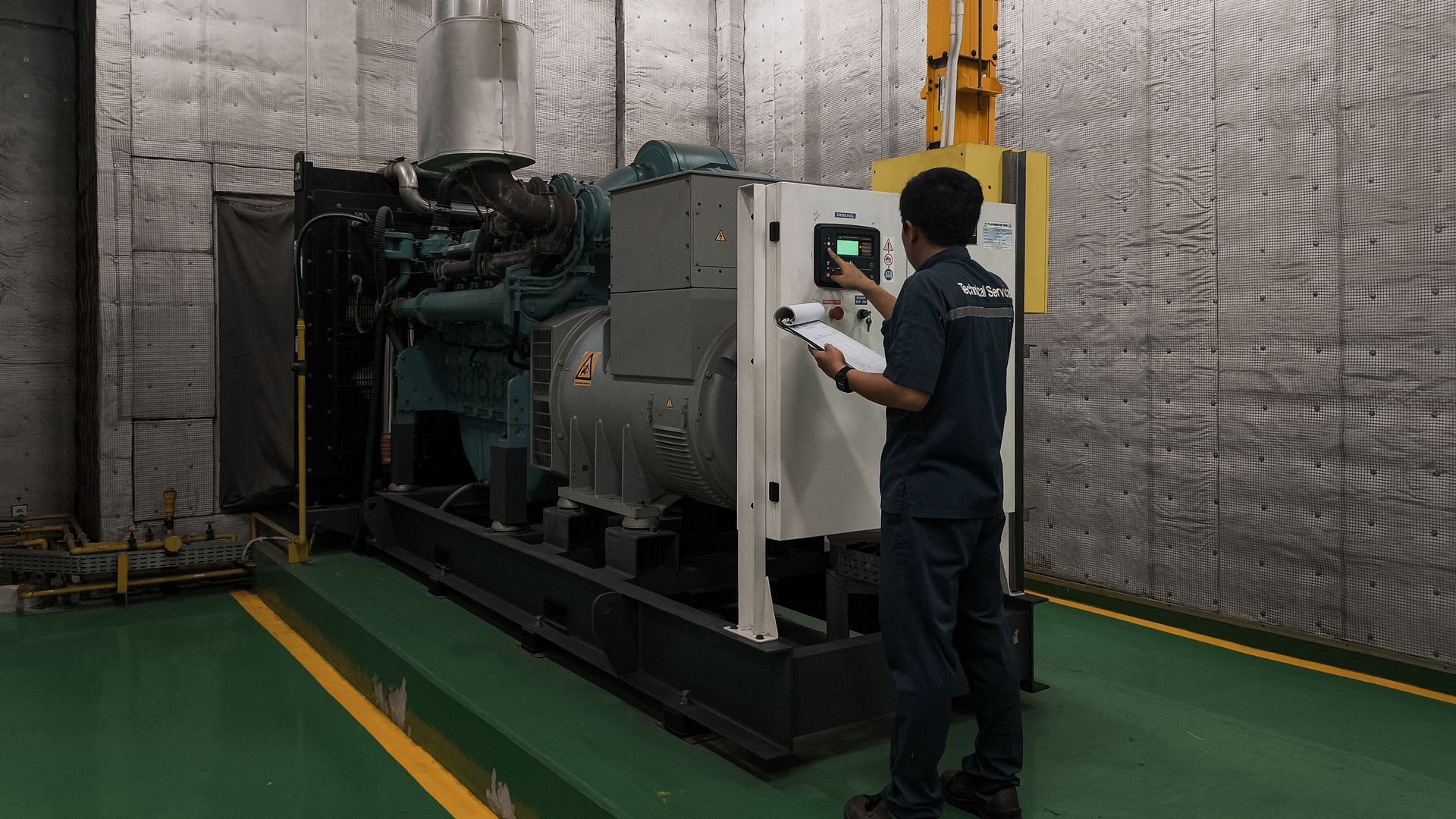 A technician records data from the control panel of a large industrial generator in a utility room.