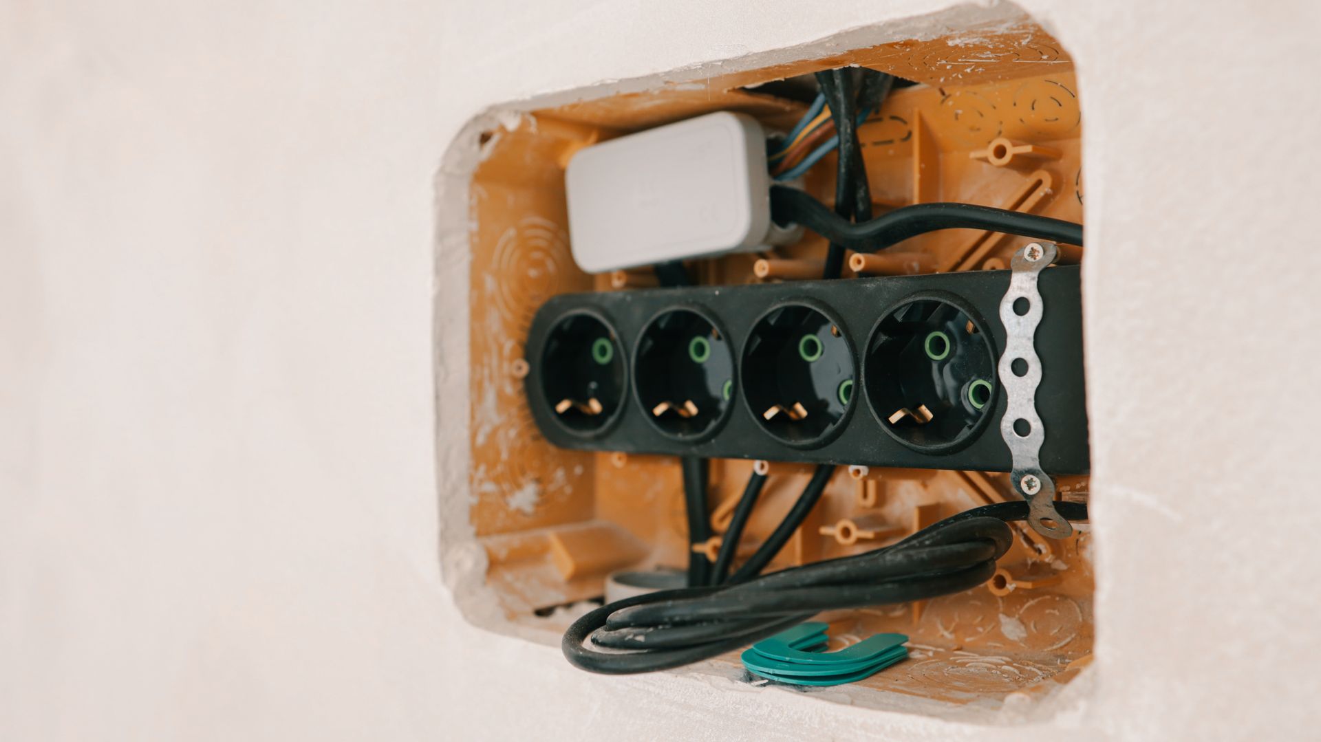 Wall-mounted electrical outlet strip with black sockets and exposed wiring in a white wall cutout