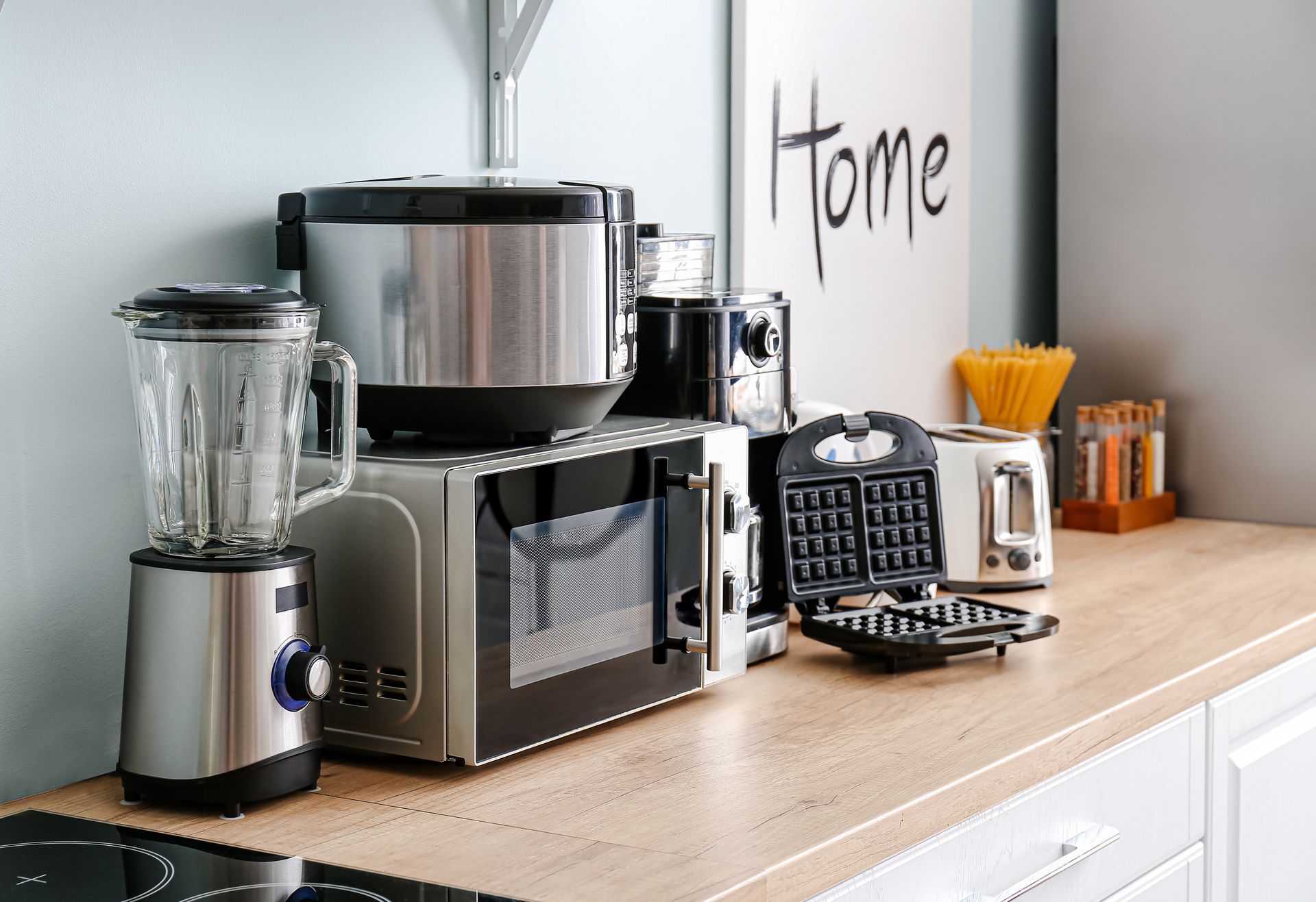 A kitchen counter features a blender, microwave, rice cooker, waffle maker, and toaster, with a