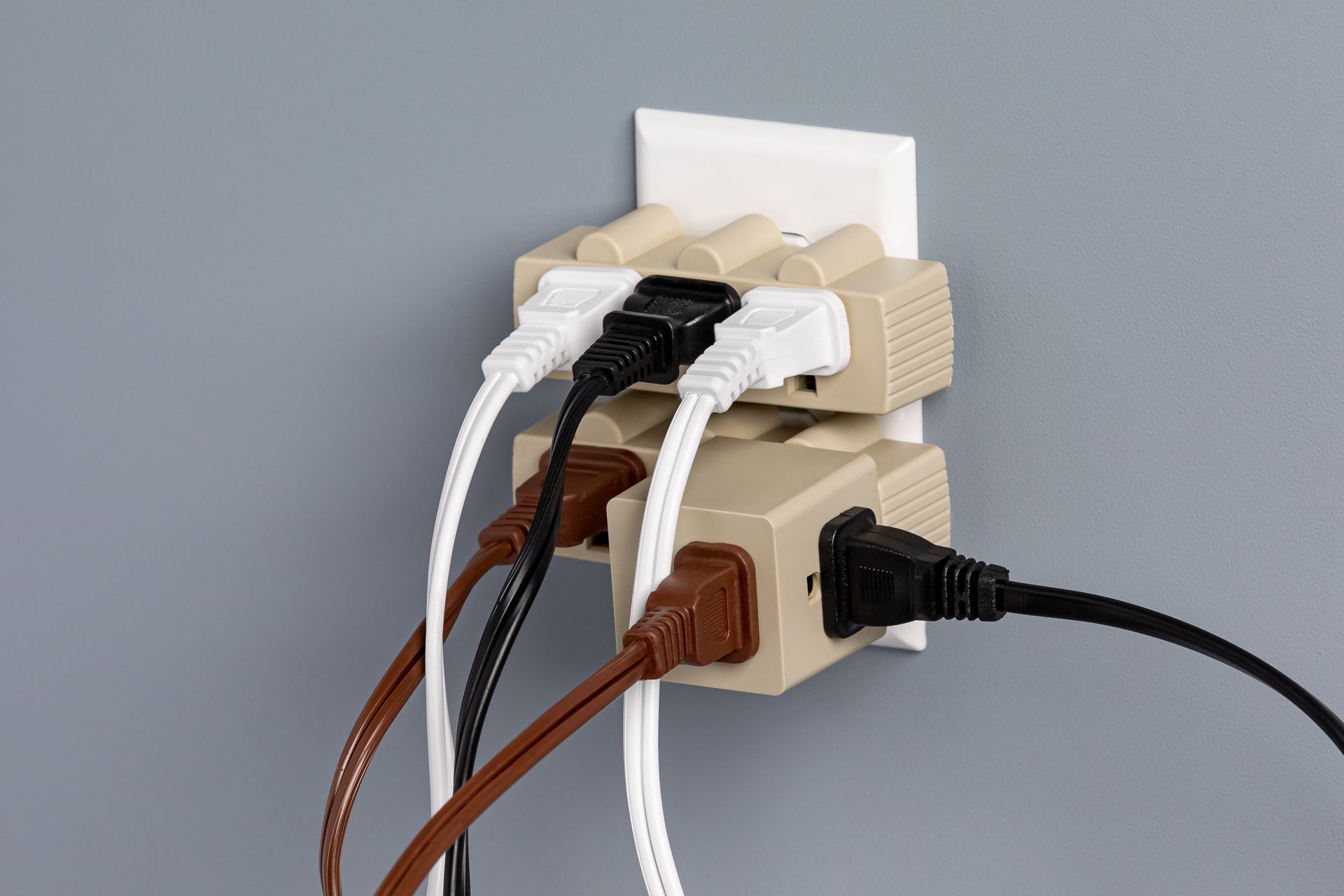 Multiple cables plugged into a wall-mounted outlet splitter on a gray wall.