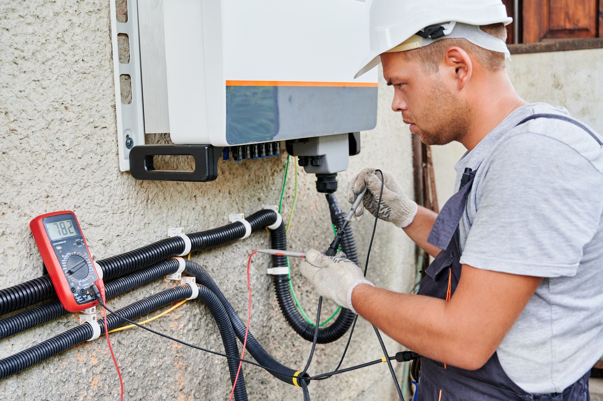 Technician inspecting outdoor electrical wiring beside a wall-mounted unit