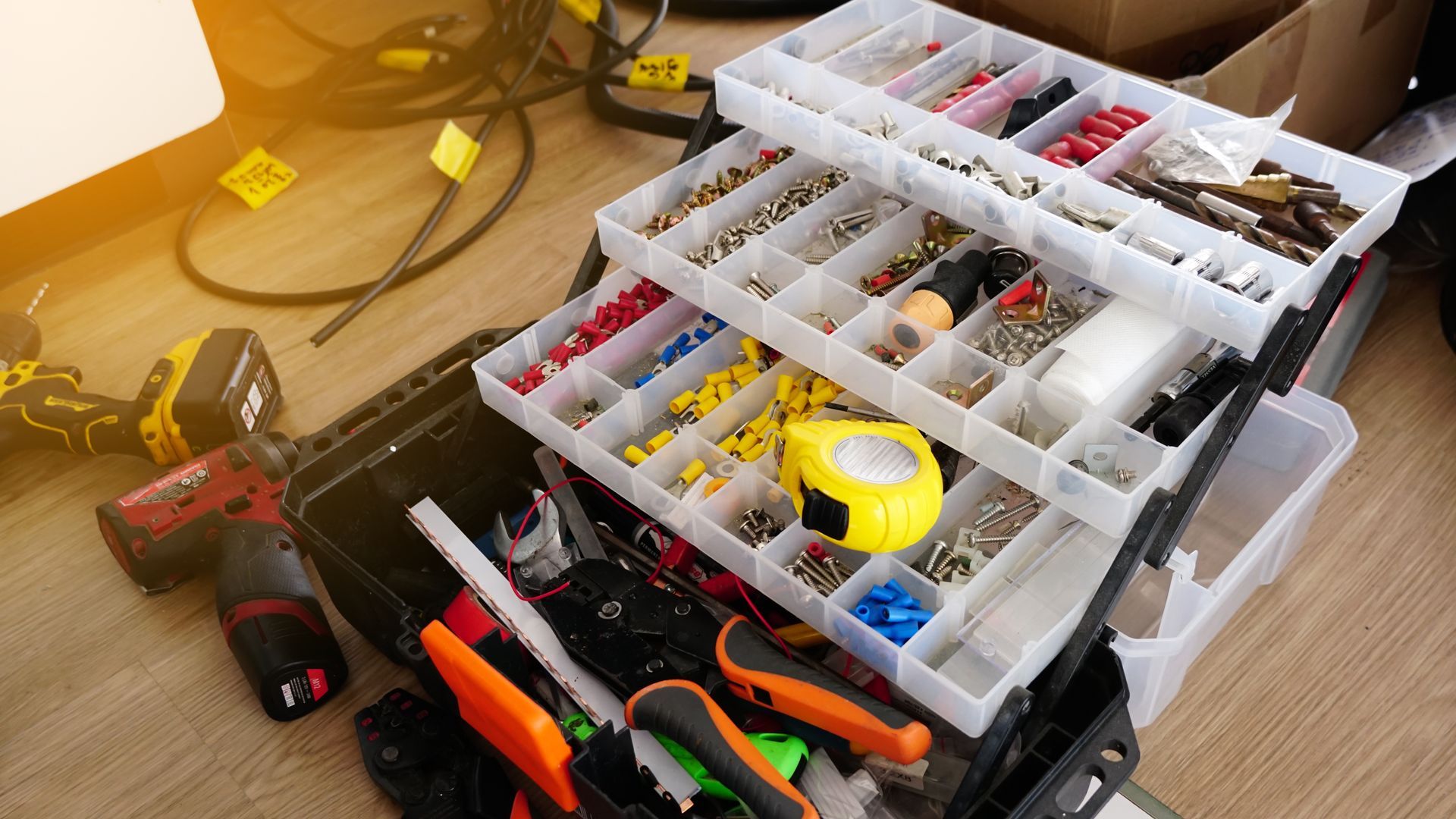 An open black toolbox with tiered clear plastic organizers filled with various electrical connectors and a tape measure.