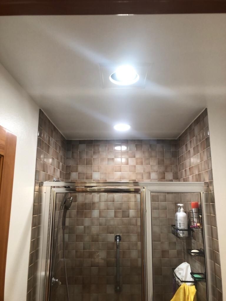 Bathroom shower with glass doors, tiled walls, and bright ceiling lights.