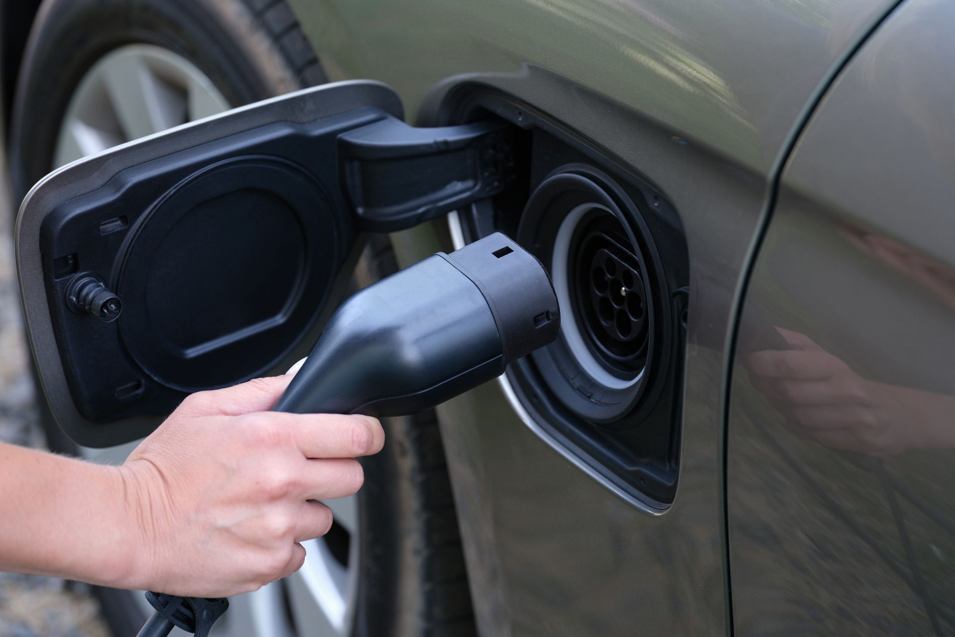 Hand plugging an EV charger into a car’s charging port with the fuel door open