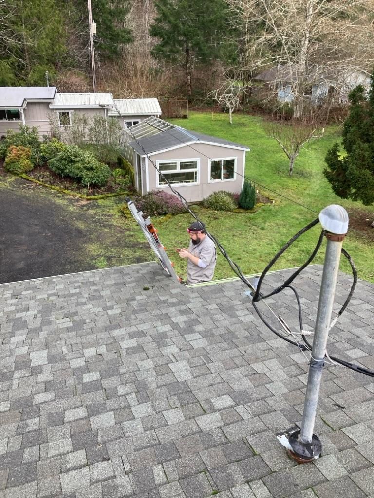 Worker on a rooftop near a ladder and satellite dish, viewed from above in a suburban yard.
