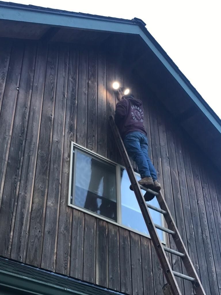 Worker on a ladder repairing the dark wooden siding of a house near the roofline
