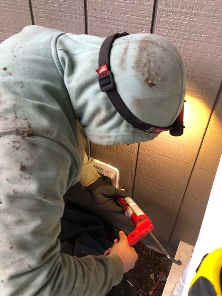 Worker in gray hoodie using a red drill to install something near a wall outlet.