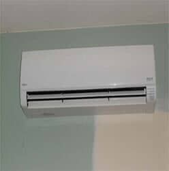 A white wall-mounted air conditioner unit positioned on a wall painted with a light green and off-white split color scheme.
