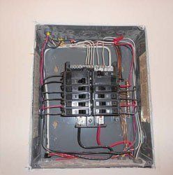 An open electrical service panel showing multiple breakers, wiring, and bus bars mounted on a wall.