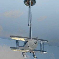 A small biplane model suspended from a ceiling against a light blue, cloudy backdrop.
