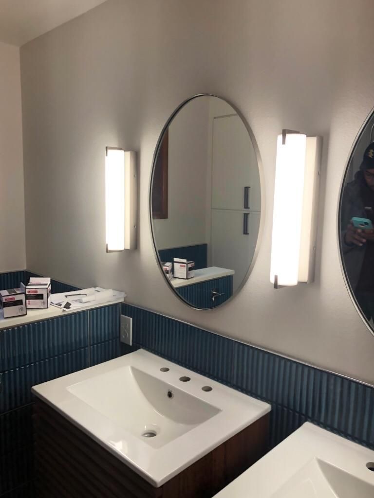 Modern bathroom with white sink, oval mirror, and wall sconces on striped blue wainscoting.