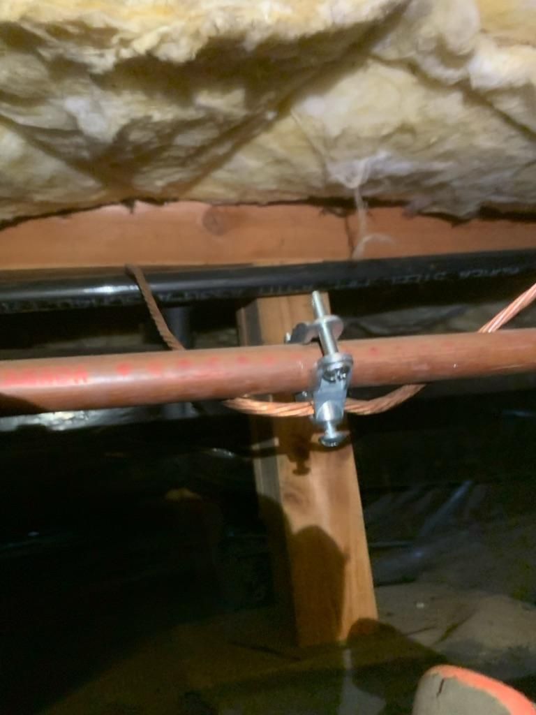 Exposed basement plumbing with copper pipe, clamp, and insulation under a floor joist.