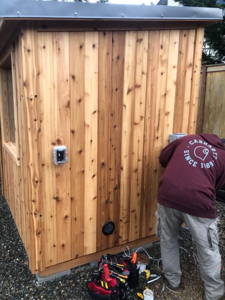 Person working beside a small wooden shed with tools on the ground