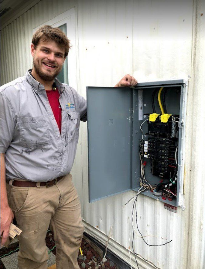 Technician standing beside an open electrical panel on a white exterior wall