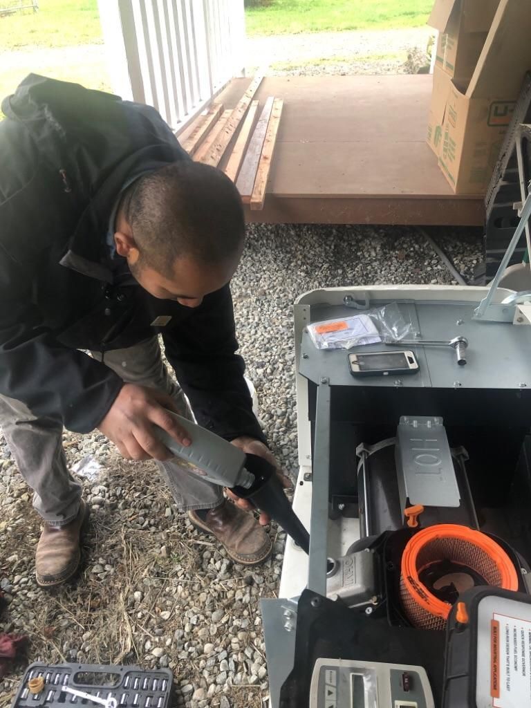 Man crouching beside an open HVAC unit, inspecting wiring with tools outdoors.