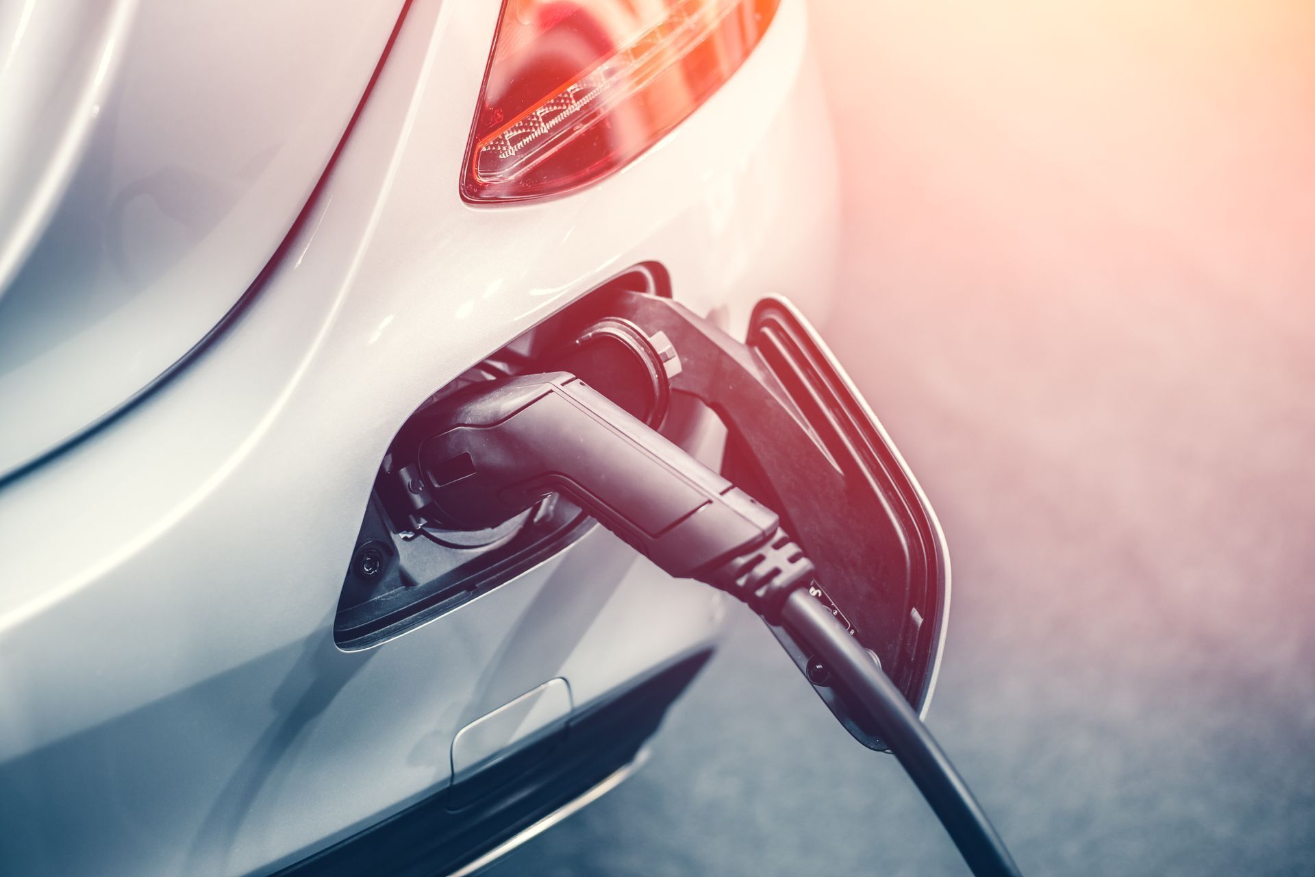 Electric car charging at a station, with a cable plugged into a white vehicle’s rear port.