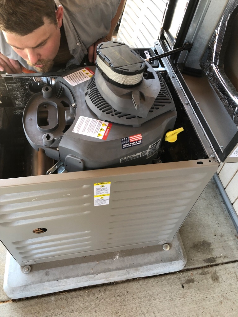 A person inspecting the engine of an open outdoor standby generator mounted on a concrete pad. A person inspecting the engine of an open outdoor standby generator mounted on a concrete pad.