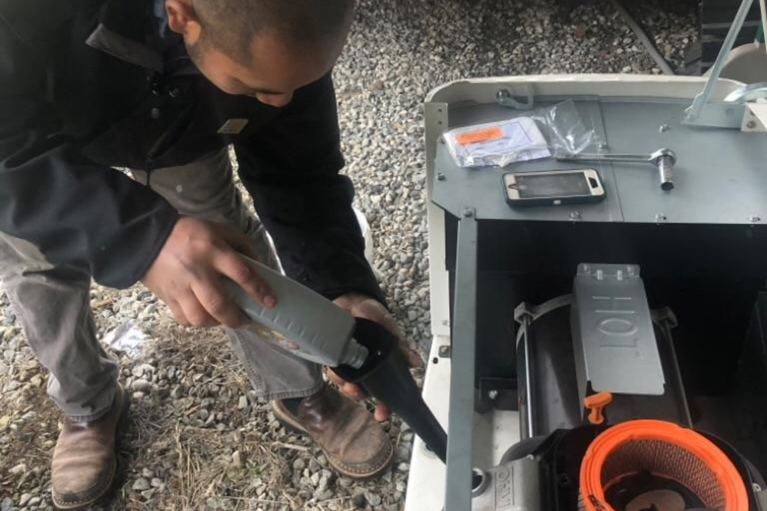 A person pouring oil into a generator engine through a black funnel.