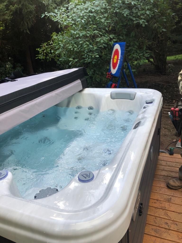 Hot tub bubbling outdoors beside a target board in a wooded backyard