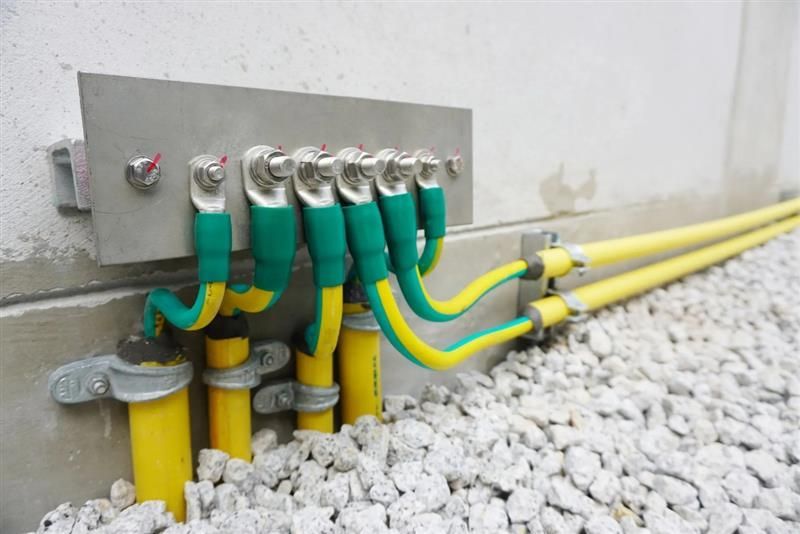 Yellow electrical cables with green grounding wires connected to a wall-mounted grounding bar outdoors.