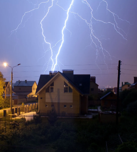 Lightning striking above houses at night in a stormy neighborhood