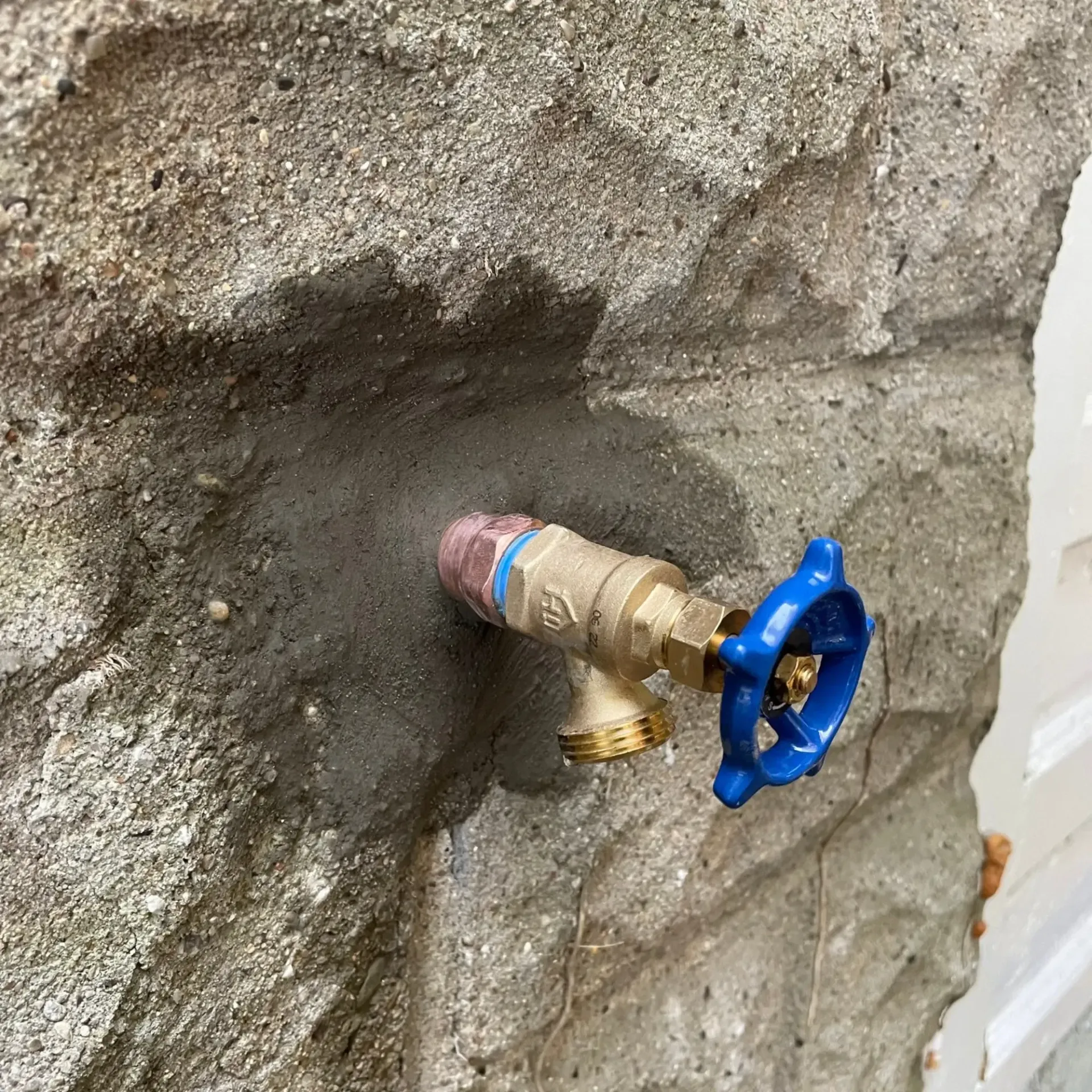 Outdoor spigot with blue handle, set in a stone wall, dripping water.