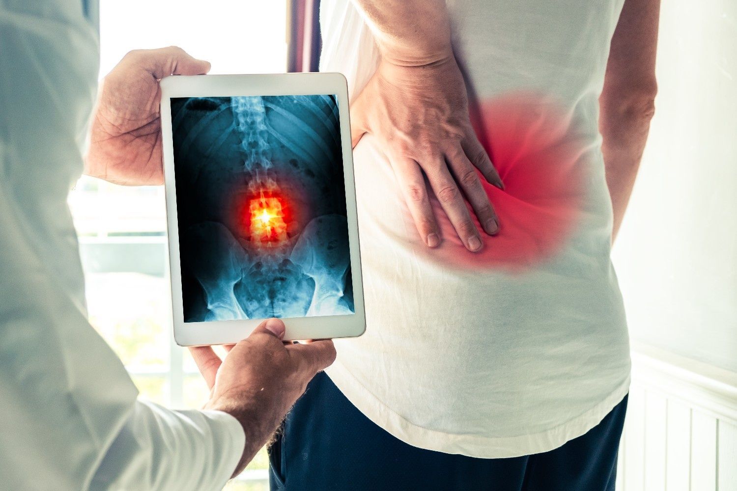 Doctor Showing an X-Ray of A Spine on A Tablet to A Patient with A Red Pain Spot on Their Lower Back — My Chiropractor Mackay City in Mackay, QLD