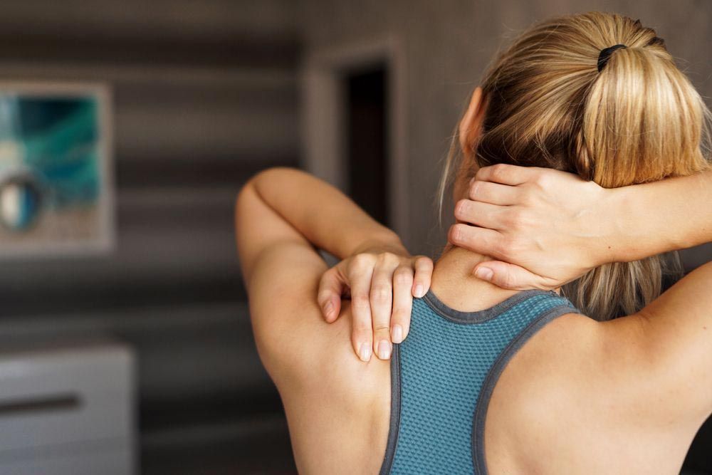 Woman in Blue Sports Bra Holding Her Neck and Shoulder — My Chiropractor Mackay City in Mackay, QLD
