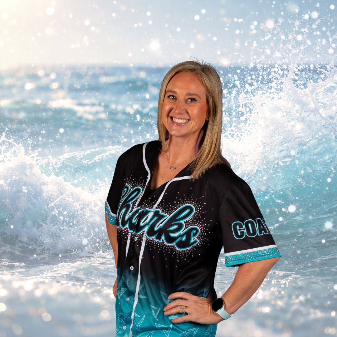 Woman in a Sharks jersey smiles, standing against a backdrop of ocean waves.