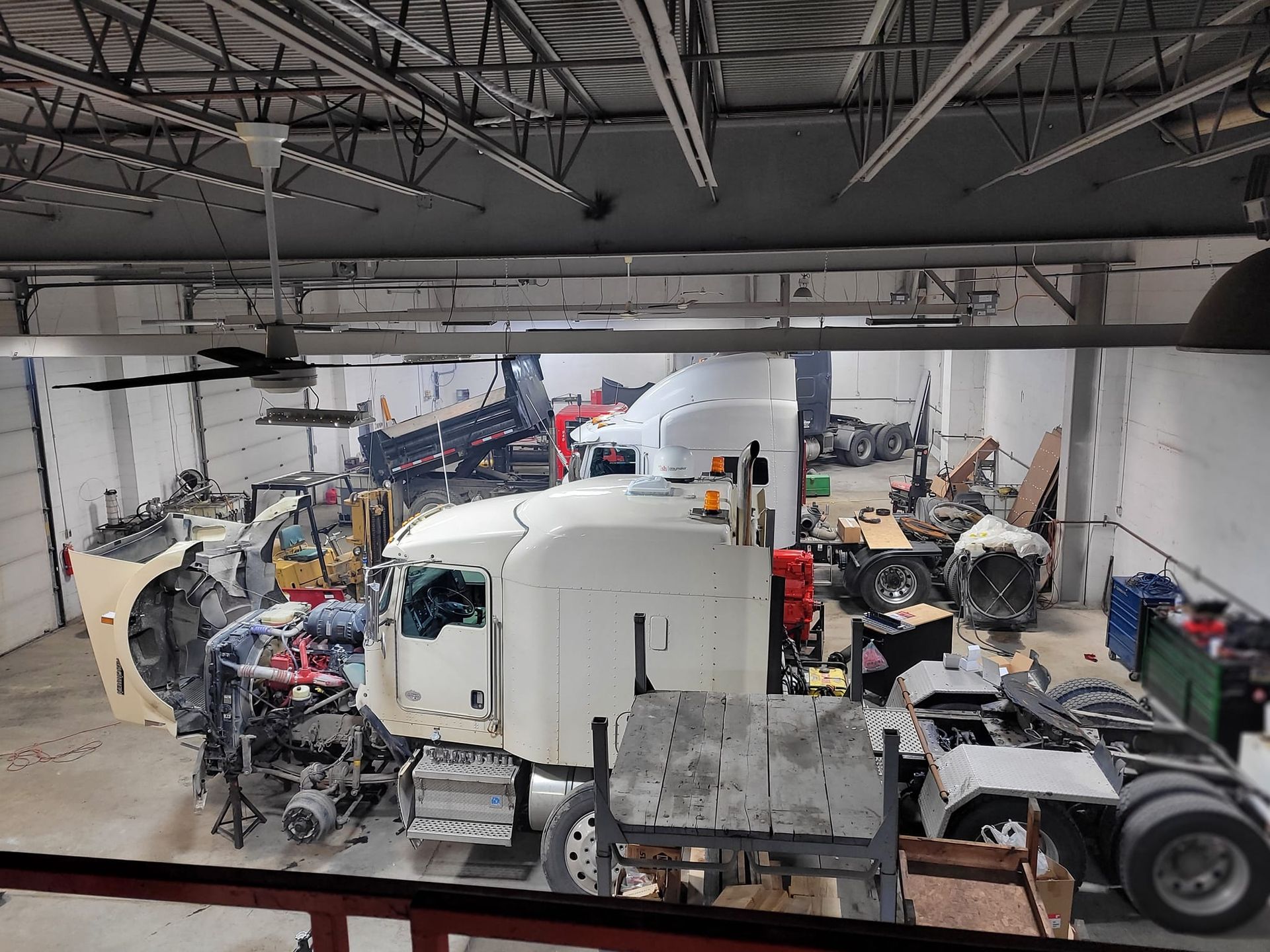 A white semi-truck cab in a workshop, surrounded by various truck parts and equipment.