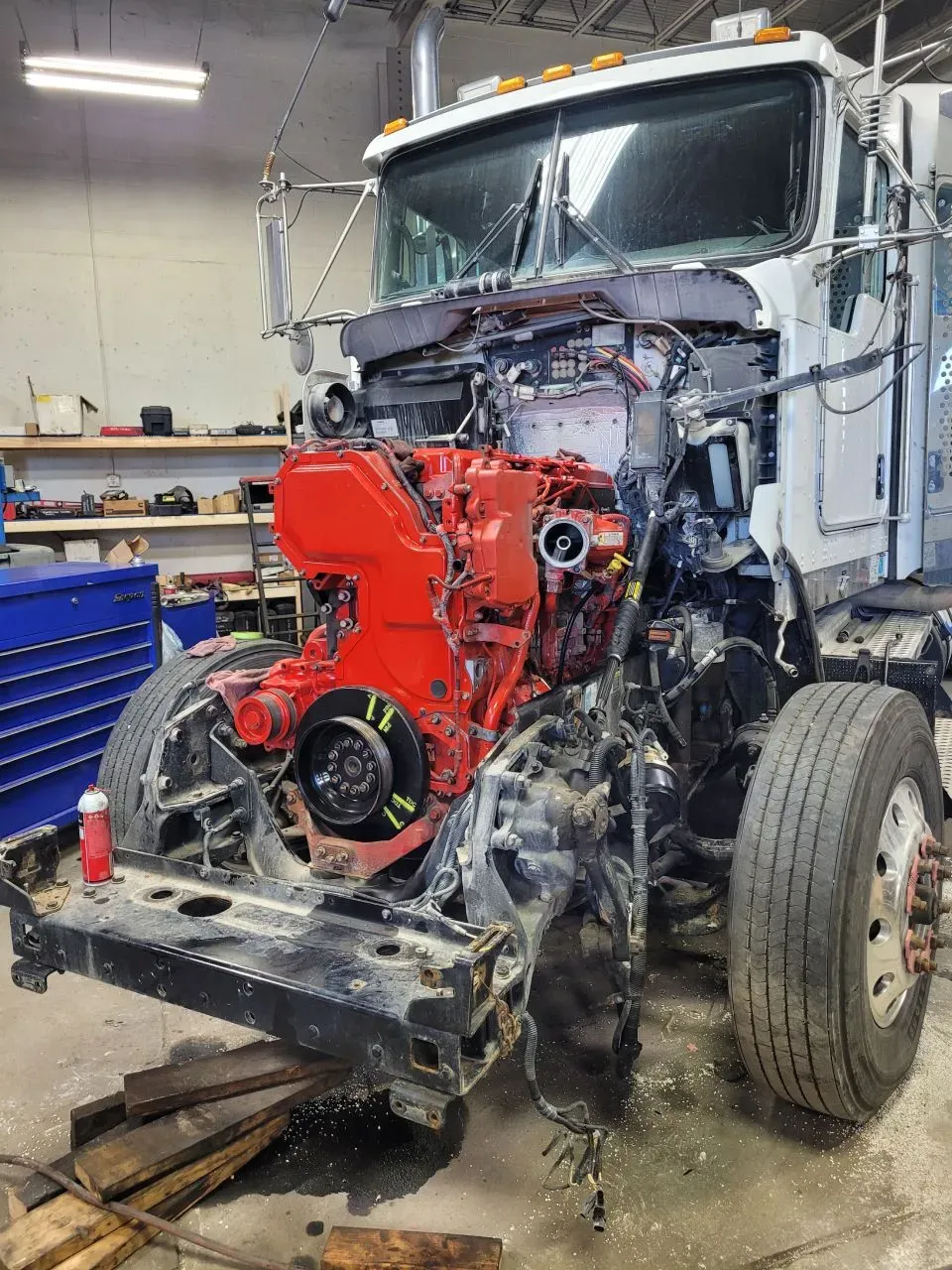 A disassembled white semi-truck in a garage, with its red engine exposed and the hood removed.