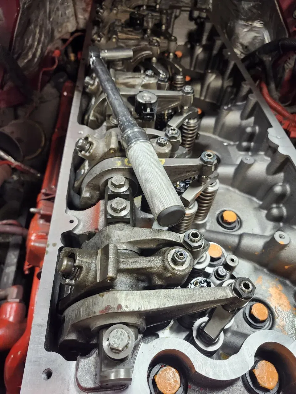 A top-down view of a vehicle engine's open cylinder head with metal rocker arms and a torque wrench resting on top.