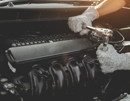 Gloved hands polishing a car engine with a handheld buffer in the engine bay