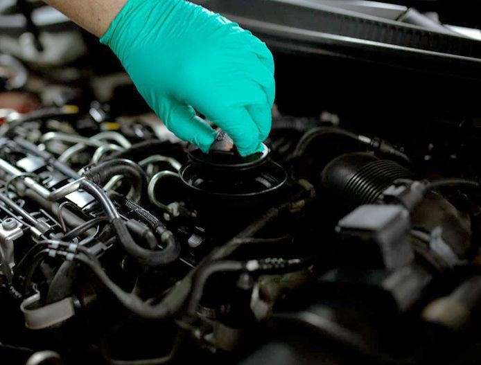 Green-gloved hand checking a car engine in a dark engine bay