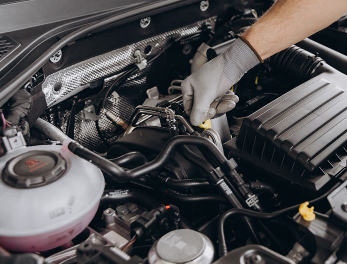 Mechanic wearing gloves inspecting a car engine with a wrench under the hood