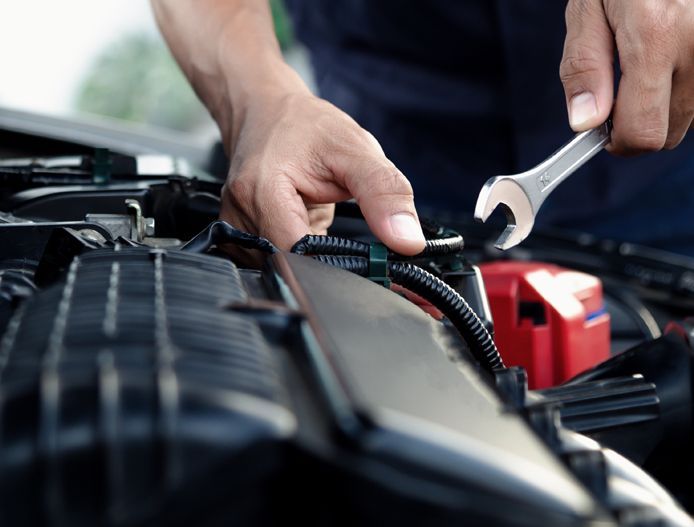 Hands using pliers to repair wiring in a car engine bay