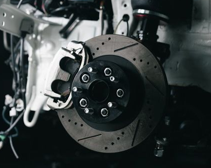 Close-up of a car brake disc and caliper assembly in a garage, with exposed suspension parts