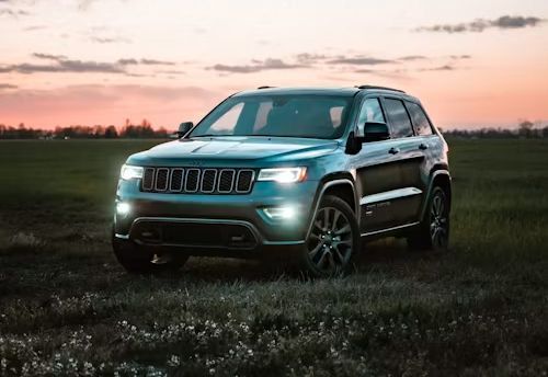 Black SUV parked in a grassy field at sunset with headlights on