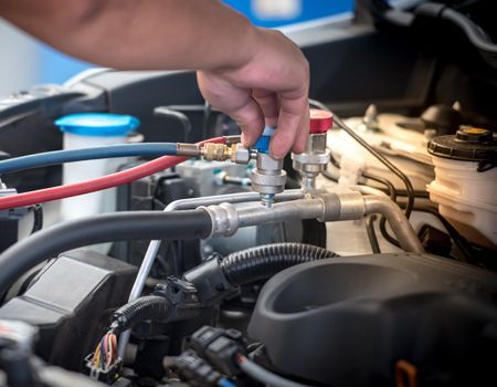 Hand adjusting car engine fittings with colored hoses in a mechanic’s bay