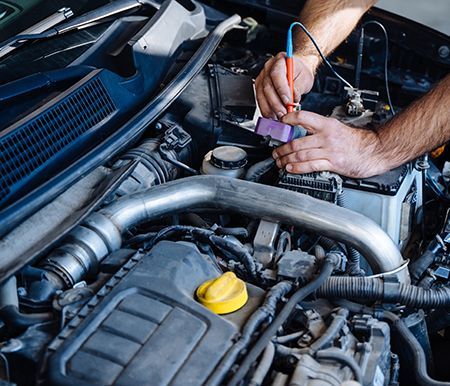 Mechanic working under a car hood with tools and wires in an engine bay