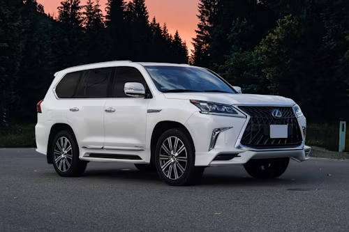 White Lexus SUV parked on a road at dusk with dark trees and pink sky in the background