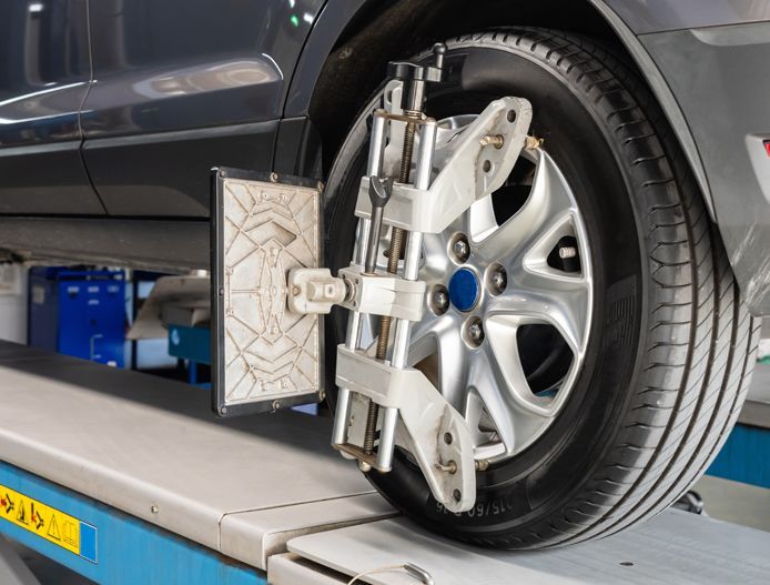 Car wheel on an alignment machine in a garage, with metal clamps attached to the rim.
