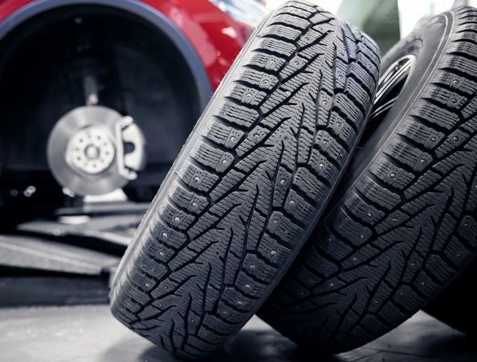 Two car tires leaning against a wheel in a garage, with a red vehicle in the background