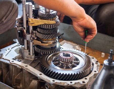 Mechanic repairing a gearbox, with gears exposed and a hand using a tool on the assembly.