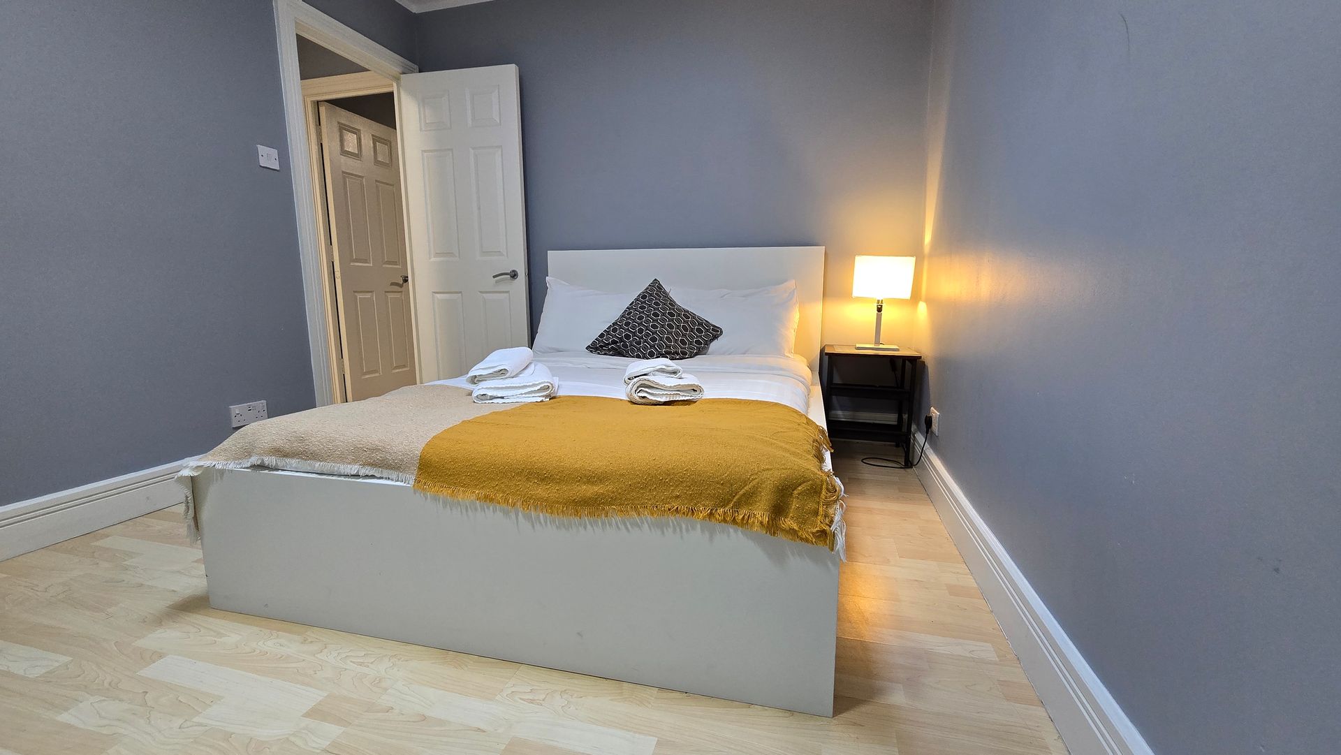 A bedroom with a bed , nightstand , lamp and door.